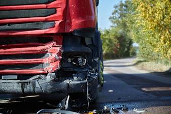 Close up of the front of a red semi truck with collision damage. 